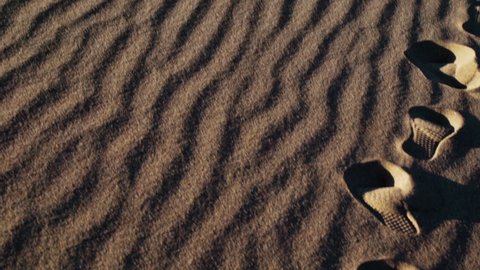 Patterns and footprints on sand dunes, sunny day - slowmo, tilt up view