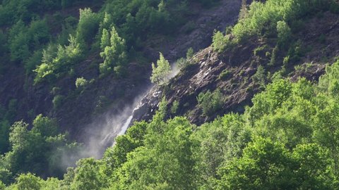 One of the waterfalls in the Naeroy fjord. A powerful torrent of water falling from the cliff, raising foam and water spray in the air. Lush green vegetation covers the mountainsides.