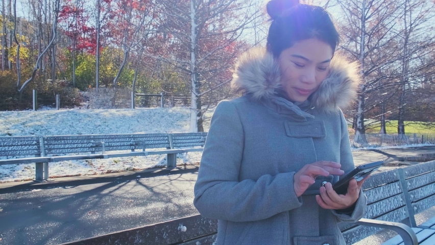 young asian female traveller hand use smartphone device communication with background of winter park in newyork united states