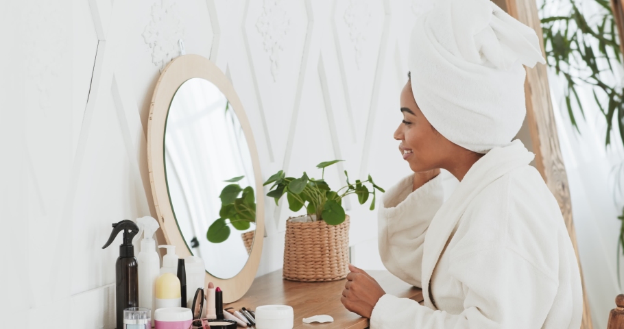 Portrait of happy attractive african american woman applying cream on face and smiling at camera, sitting after shower in bathroom, slow motion Royalty-Free Stock Footage #1062422653