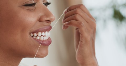 Intensive tooth care. Young black woman flossing her teeth with tooth floss at home, close up portrait