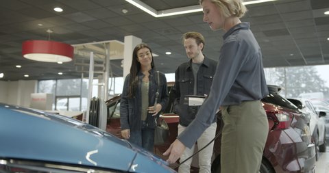 Sales Woman demonstrating charging electric car to couple in car showroom