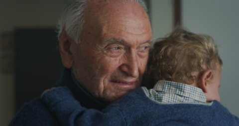 Cinematic close up shot of senior gray hair grandfather is cuddling a grandson baby while sleeping peacefully on  his arms at home.Concept of life, grandparents, love, care, generation, childhood