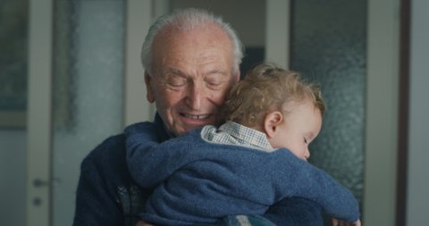 Cinematic shot of tender senior gray hair grandfather is cuddling a grandson baby while sleeping peacefully on  his arms at home.Concept of life, grandparents, love, care, generation, childhood