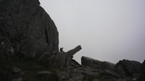 A man climbing onto a dangerous mountain ledge on Tryfan mountain in Snowdonia