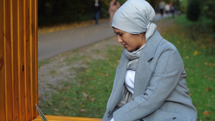 Young muslim woman with laptop sitting on a park bench