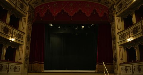 Cinematic shot of empty classic theatre with red velvet curtains opening stage with dramatic lighting before start of show.