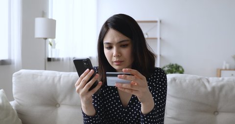 Stressed millennial asian vietnamese mixed race woman making online payments using bank card and mobile applications, feeling unhappy with wrong data enter or financial problems in e-banking account.