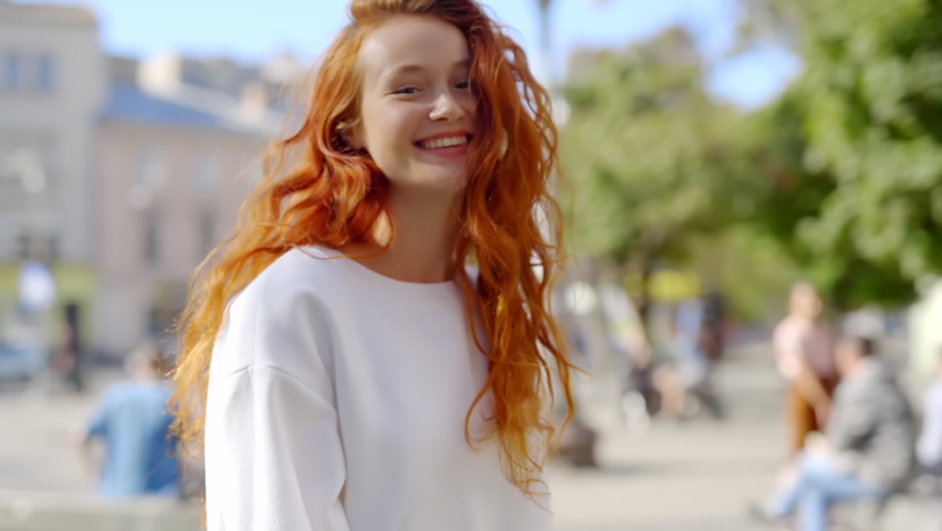 Portrait young sunshine woman with red hair turning look at camera smile stand in the city streets. Beautiful face emotion lifestyle. Portrait outdoor close up. Slow motion Royalty-Free Stock Footage #1062432205