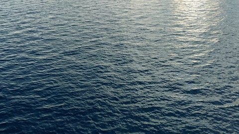Camera hangs over the blue open calm sea water 