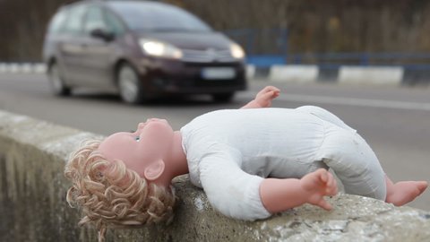 A baby doll lies on the side of a highway.Abandoned doll on the road.
