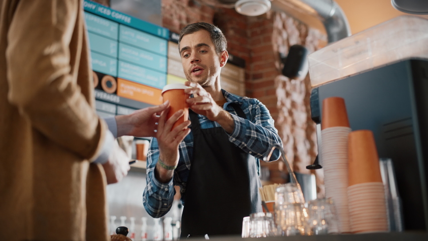 Tall Caucasian Customer Pays for Coffee and Pastry with Contactless NFC Payment Technology on Smartphone to a Handsome Barista in Blue Checkered Shirt. Contactless Mobile Payment in Cafe Concept. | Shutterstock HD Video #1062436996