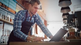 Young and Handsome Coffee Shop Owner is Working on Laptop Computer and Checking Inventory in a Cozy Cafe. Happy Restaurant Manager in Checkered Shirt Browsing Internet and Chatting with Friends. - Powered by Shutterstock - Get 15% off with code: PIKWIZARD15
