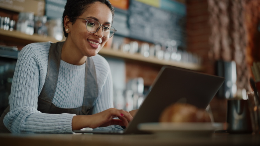 Young and Beautiful Latina Small Business Owner is Working on Laptop Computer and Checking Inventory in a Cozy Cafe. Happy Restaurant Manager or Employee Browsing Internet and Chatting with Friends. | Shutterstock HD Video #1062437047