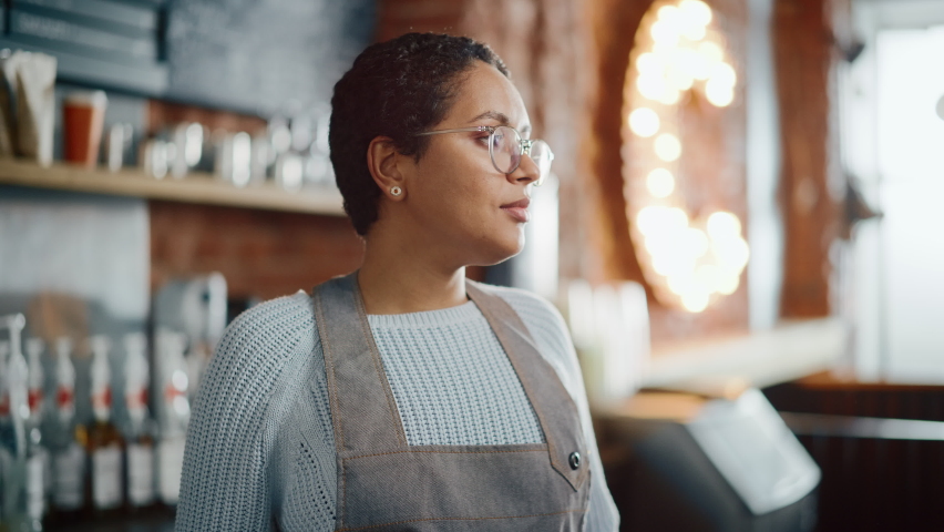 Beautiful Latin American Female Barista with Short Hair and Glasses is Projecting a Happy Smile in Coffee Shop Bar. Portrait of Happy Employee Behind Cozy Loft-Style Cafe Counter in Restaurant. Royalty-Free Stock Footage #1062437071