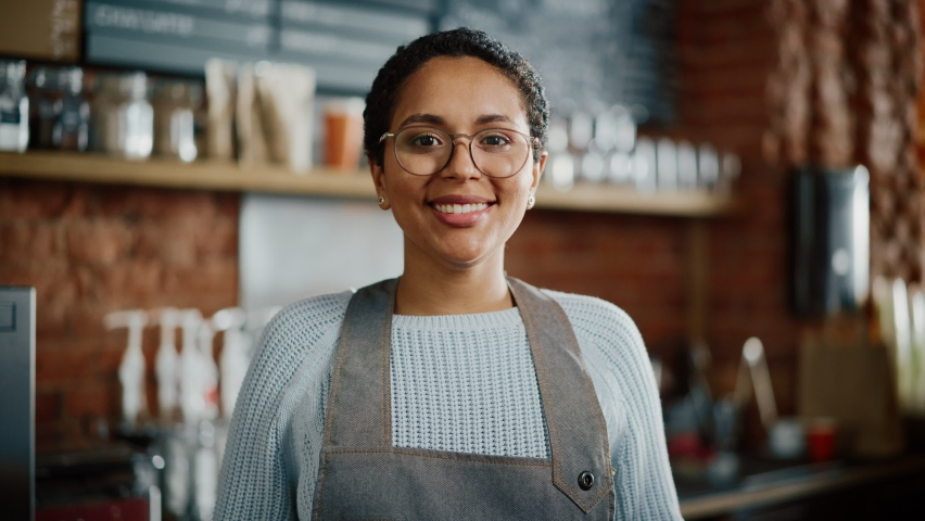 Beautiful Latin American Female Barista with Short Hair and Glasses is Projecting a Happy Smile in Coffee Shop Bar. Portrait of Happy Employee Behind Cozy Loft-Style Cafe Counter in Restaurant. Royalty-Free Stock Footage #1062437071
