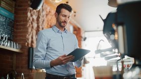 Handsome Caucasian Coffee Shop Owner is Working on Tablet Computer and Checking Inventory in a Cozy Loft-Style Cafe. Successful Restaurant Manager Standing Happy Behind Counter and Smiles on Camera. - Powered by Shutterstock - Get 15% off with code: PIKWIZARD15