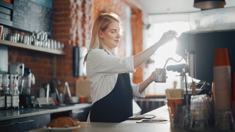 Beautiful Young Caucasian Barista with Blond Hair is Making a Cup of Fresh Coffee in a Cafe. Happy and Smiling Bar Employee Posing while Working in a Cozy Loft-Style Coffee Shop Restaurant Counter. Video de stock