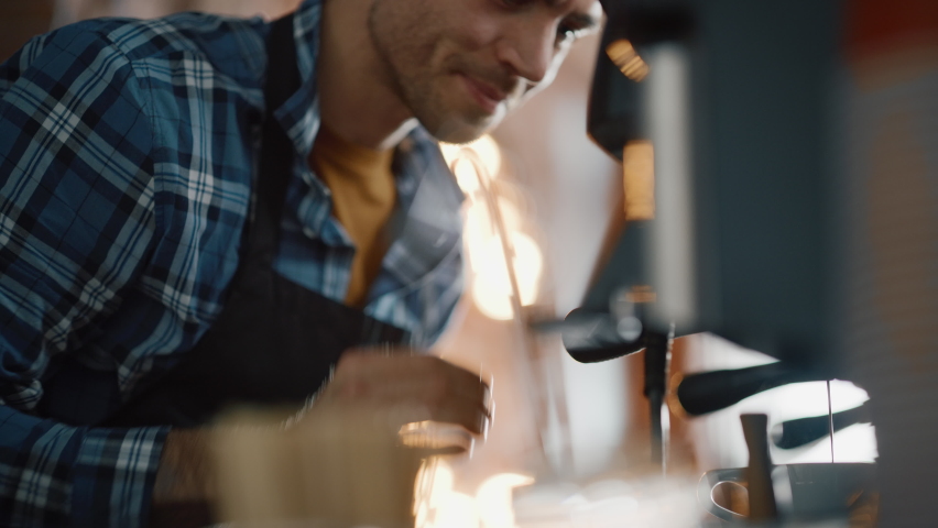 Close Up Portrait of a Handsome Male Barista in Checkered Shirt Making Cappuccino in a Coffee Shop Bar. Small Business Owner Works at a Cozy Loft-Style Cafe Counter and Loves His Job. Royalty-Free Stock Footage #1062437164