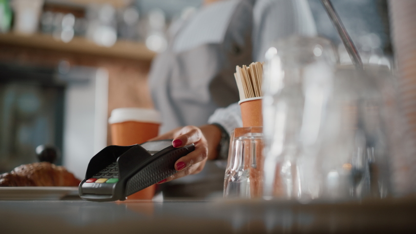 Close Up of a Feminine Hand Holding a Smartphone with an NFC Payment Technology Used for Paying for Take Away Coffee in a Cafe. Customer Uses Mobile to Pay for Latte Through a Credit Card Terminal. Royalty-Free Stock Footage #1062437257