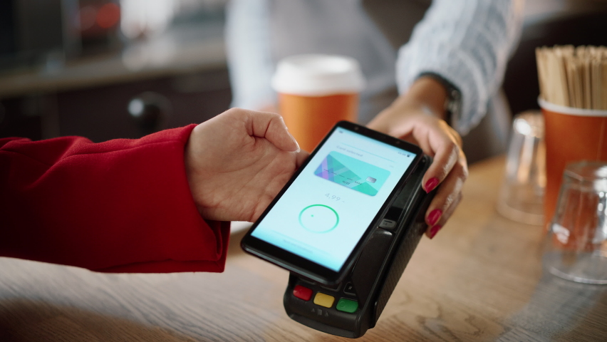 Close Up of a Feminine Hand Holding a Smartphone with an NFC Payment Technology Used for Paying for Take Away Coffee in a Cafe. Customer Uses Mobile to Pay for Latte Through a Credit Card Terminal. - Powered by Shutterstock - Get 15% off with code: PIKWIZARD15