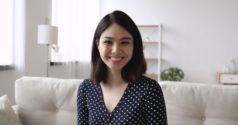 Web camera view happy young korean asian mixed race woman sitting on sofa, involved in distant video call conversation with friends or passing job interview remotely from home, feeling confident.