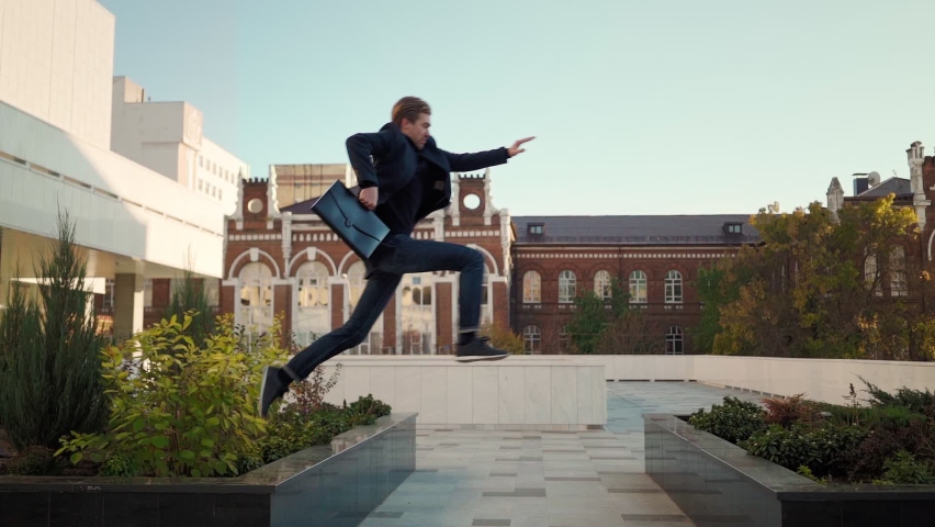 Happy successful business man with folder documents jumping over an obstacle on the city background. Overcoming difficulties on the way. Young entrepreneur takes a step towards success. Slow motion. | Shutterstock HD Video #1062439141