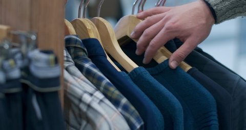Close-up of male Caucasian hand choosing shirts hanging on rack in clothing shop. Unrecognizable man buying clothes in shopping mall. Cinema 4k ProRes HQ.