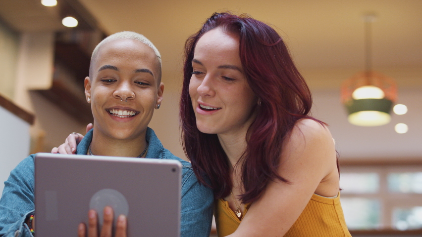 Same sex female couple using digital tablet to stream online as they sit at home together