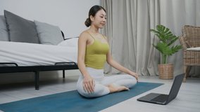 Asian woman practicing yoga online on laptop at home. meditating alone on the floor with eyes closed, Yoga, balance, meditation, relaxation, healthy lifestyle, self-care, online training class concept