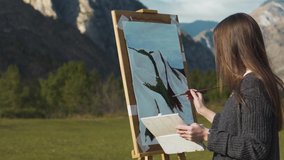 Beautiful girl paints a picture in the mountains. A professional artist creates a landscape on a molbert. Hobbies, hobbies and work in the fresh air. Close-up 4K video.