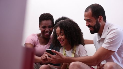 Family looking at smartphone together, mixed race parents and kids holding cellphone at home
