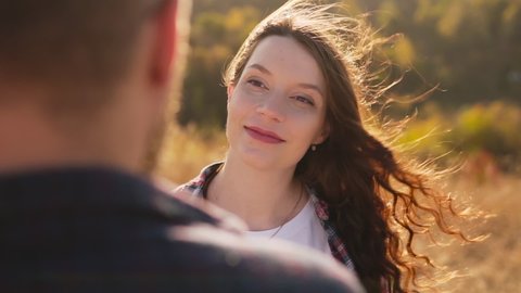 A young girl looks lovingly into the eyes of her boyfriend husband, the wind caresses her hair. Shoot from behind the shoulder of her boyfriend. Love and relationships. Close-up, slow motion. 