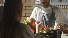 Cheerful male farmer in apron and cap smiling and giving crate with fresh produce, bread and milk to female customer while doing farm-to-door delivery service - Powered by Shutterstock - Get 15% off with code: PIKWIZARD15