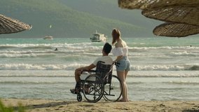 Disabled young man, the women he loves, looking at the sea. They enjoy the view. Slow motion video.