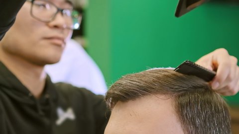 Concentrated barber in trendy glasses holds professional tools in hands combs and dries hair extreme close view slow motion