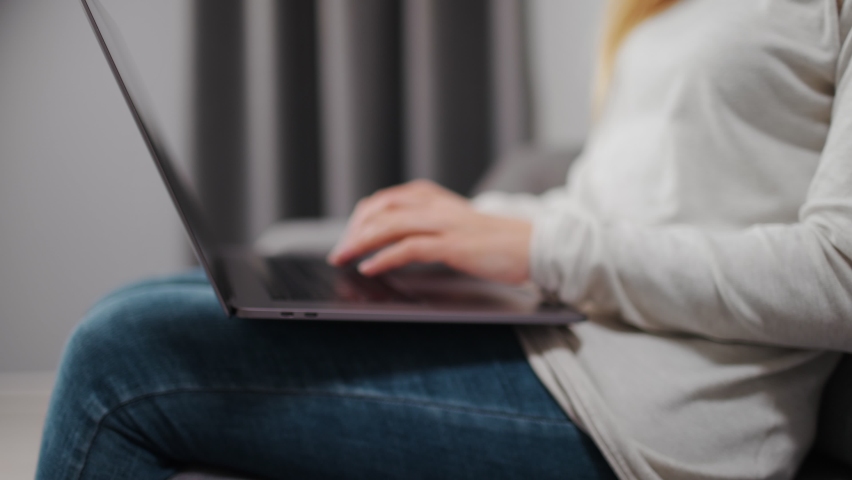 Relaxed woman in domestic outfit sitting on grey couch and typing on wireless laptop. Close up of female hands and keyboard. Concept of modern gadget. | Shutterstock HD Video #1062463891