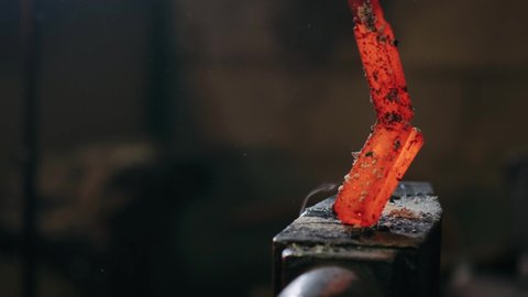 A blacksmith forges red-hot metal on an anvil. The hammer of smith beat on glowing hot metal and sparks fly in all directions. Metalworking. Blacksmithing Workshop.