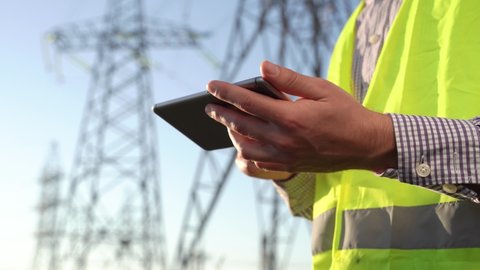 close up. engineer with smartphone working near electric poles. worker using mobile phone for checking data while standing against high voltage power towers