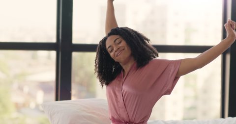 Lazy morning. Young well slept african american woman in pajamas stretching, sitting in bed, waking up, greeting new day