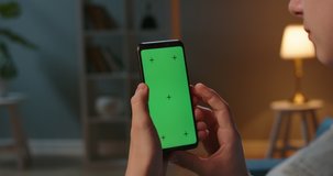 Close up shot of guy using his smart phone with mock up green screen at night, using various gestures to scroll through online shop or social media 4k video template