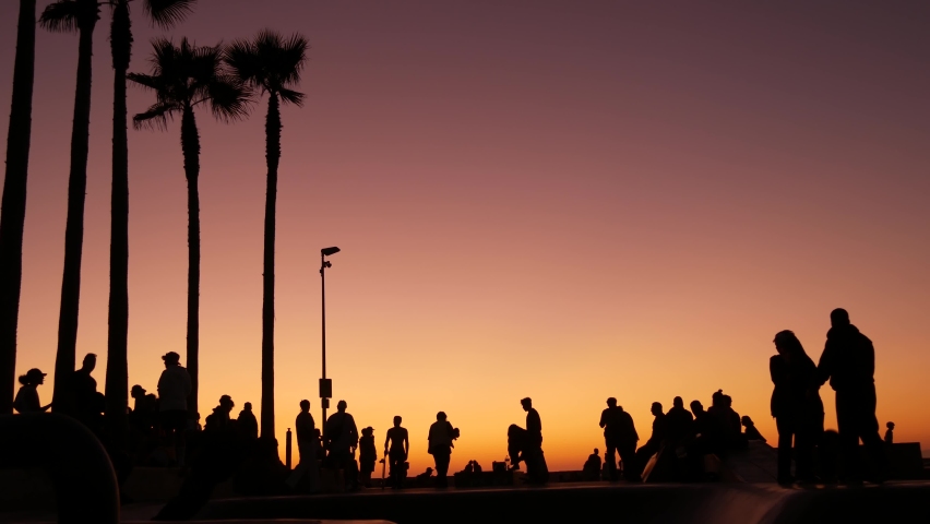 Silhouette of young jumping skateboarder riding longboard, summer sunset background. Venice Ocean Beach skatepark, Los Angeles California. Teens on skateboard ramp, extreme park. Group of teenagers
