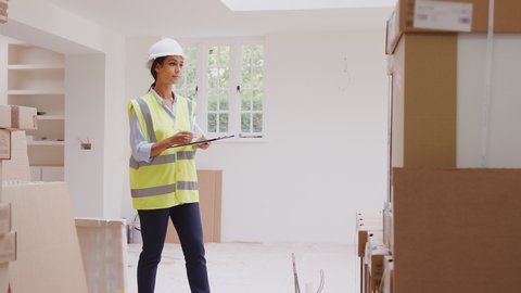 Female builder wearing hard hat with digital tablet checking delivery of new kitchen units inside property - shot in slow motion