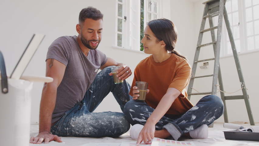 Couple sitting on floor drinking coffee wearing old clothes with paint chart ready to decorate new home - shot in slow motion Royalty-Free Stock Footage #1062490366