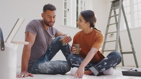 Couple sitting on floor drinking coffee wearing old clothes with paint chart ready to decorate new home - shot in slow motion - Powered by Shutterstock - Get 15% off with code: PIKWIZARD15