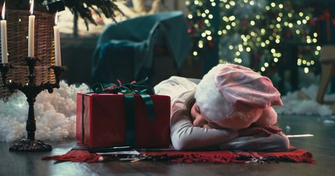 Crop Santa Claus taking letter and leaving gift near peacefully sleeping girl on Christmas eve in cozy room