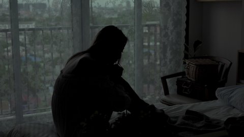 Depressed Asian woman sitting alone on the bed in the dark with cuddle herself and crying. Loneliness sad female think grief trouble life problem in bedroom. Negative emotion and mental health concept