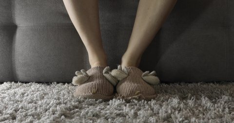 woman in slippers sits on the sofa and takes off her shoes
