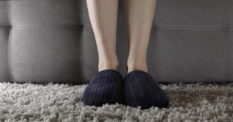 woman in slippers gets up from the couch and walks away
