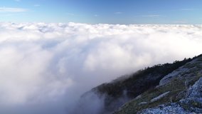 Aerial view of thick fog, like beautiful ocean of clouds and mountain peaks above clouds. Sun is rising above the endless sea of clouds until the horizon.